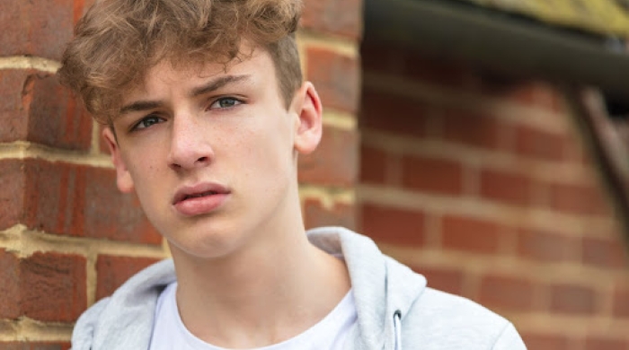 Young man stares intensely at camera while leaning against a brick wall