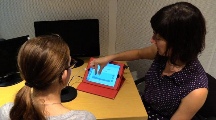 A photo of Heather Kabakoff directing a child to look at the screen of an iPad, where the staRt app is open. Below the photo are two animated stills from the app. One depicts ocean waves with the caption "Image of Poor /R/." The other shows ocean waves with the caption "Image of Good /R/."  