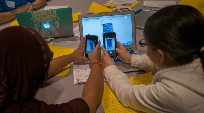 Two students use smartphones to photograph a string of code they created on a shared computer. 
