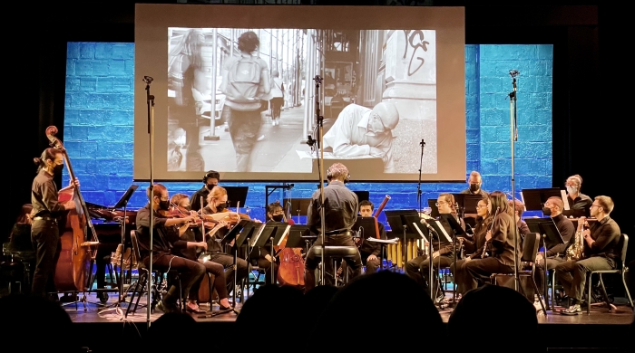 The NYU Contemporary Music ensemble featuring strings, woodwinds, brass, and percussion perform live music synchronized with a film projected on a large screen