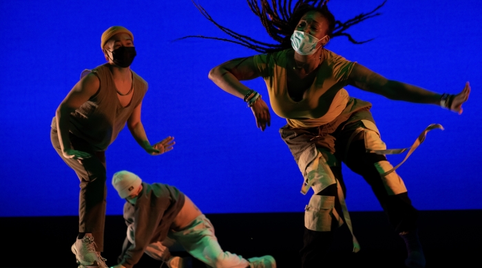 Three Dance Education performers dancing in front of bright blue background