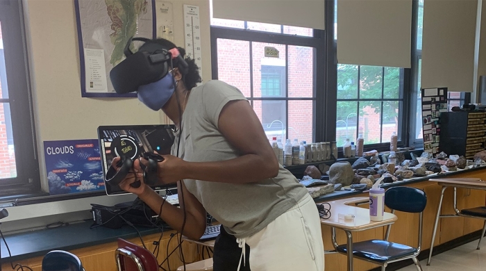 A student, wearing a VR headset, plays BOXVR in a classroom. 