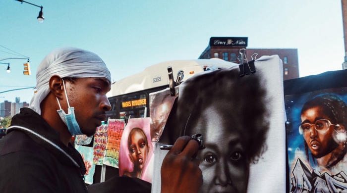 Black street artist airbrushing a portrait of a Black woman.