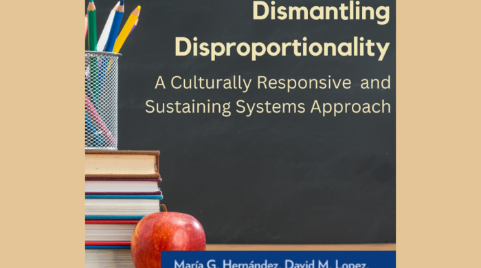 Image serves a book cover for "Dismantling Disproportionality: A Culturally Responsive and Sustaining Systems Approach " Cover image feature book title written on a chalkboard. The chalkboard is behind a teachers desk, with features books, pencil, and an apple on it.