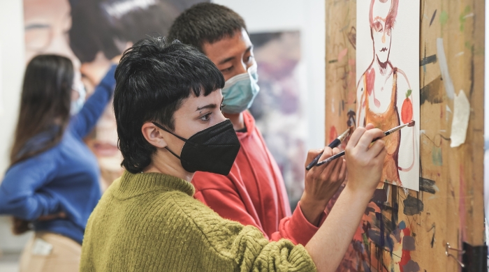 Young students painting together inside art room at school while wearing safety face mask.