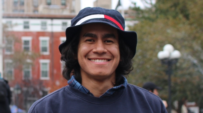 Photo of Ben in Washington Square Park; smiling, wearing a hat and navy blue sweater
