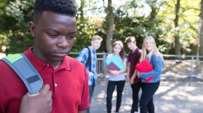 Image captures Black male student looking depressed, as his white classmates tease and bully him.