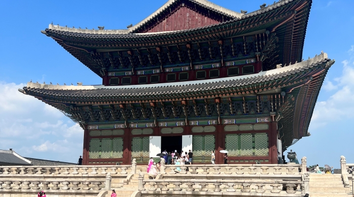 A view of Gyeongbokgung Palace in Seoul, with several people in brightly colored clothing in front of the palace.
