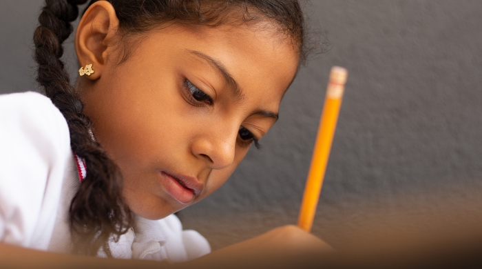 Image captures a close up photo a elementary school student using a pencil to complete an outstanding assignment.