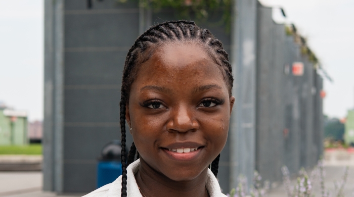 Image capture a student wearing a white shirt, as she stand in front of a bed of flowers surrounded by concrete.