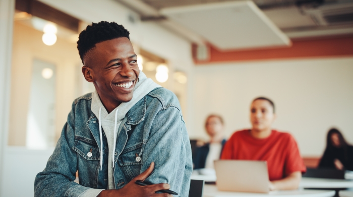 Image captures a high school student sitting at his desk in the classroom, while following the assignment in his textbook.