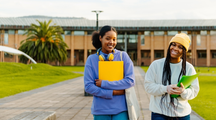 Two Black teenage girls walking down an outdoor walkway with their school books.