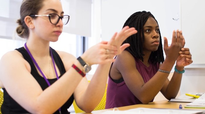 Two women mimic an occupational therapy wrist exercise in a classroom.