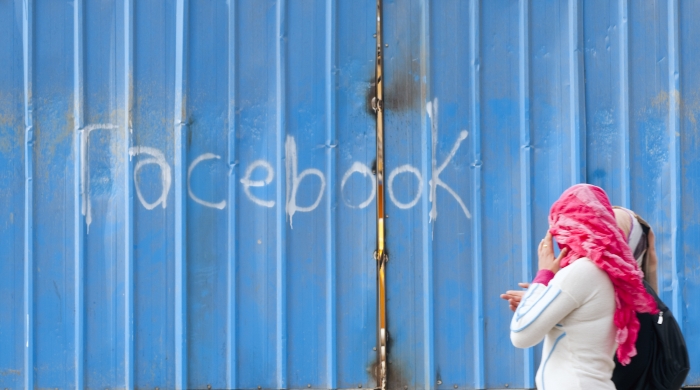 A young person in a veil walks past a blue wall with the words Facebook spray painted on