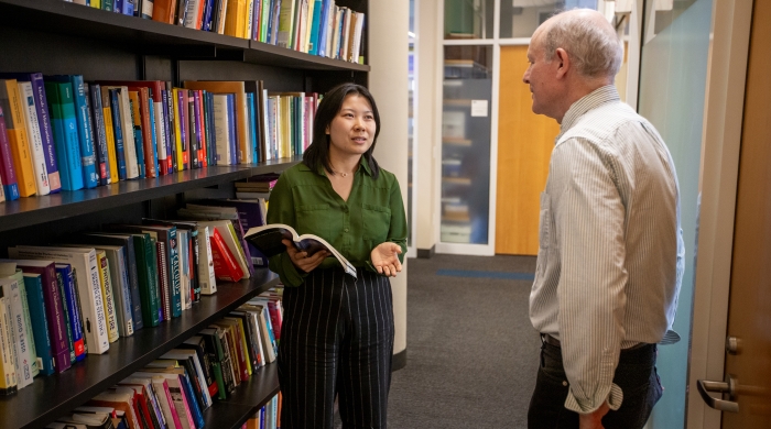 Professor Marc Scott conversing with A3SR student Nora by a bookshelf