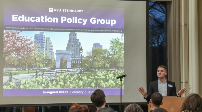 A photo of Alejandro J. Ganimian speaking at a podium in front of an audience with a slide behind him that says "NYU Steinhardt, Education Policy Group, Inaugural Event, February 7, 2024"