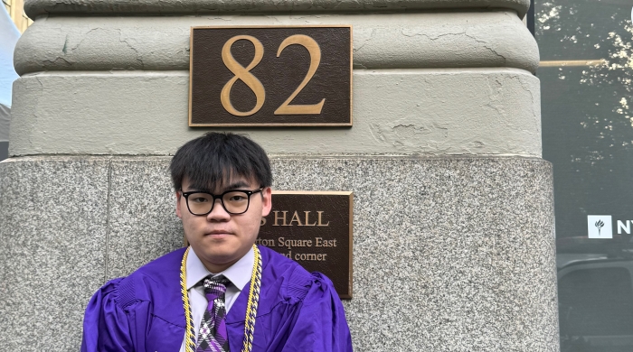 Ray Sun in violet graduation robes in front of Pless Hall