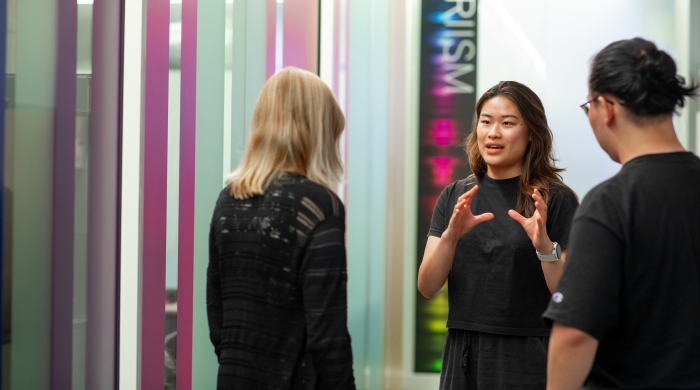 student standing, talking with two faculty members in front of a PRIISM sign