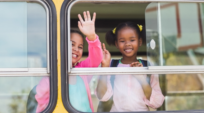 Two girls waving from a school bus.