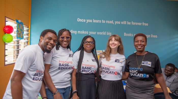 Five people wearing United Way t-shirts smile and pose in front of a blue wall