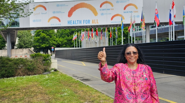 Padmini Murthy stands in front of a building, which has a poster that reads "Health for All"
