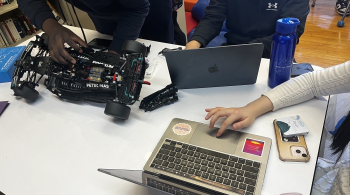 People sit around a table with laptops and robotics equipment