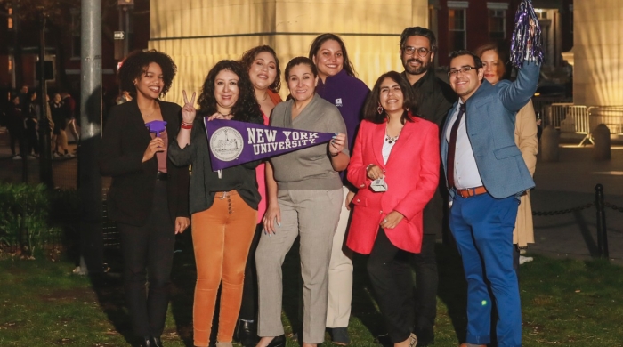 A group of people poses for the photo holding an NYU banner