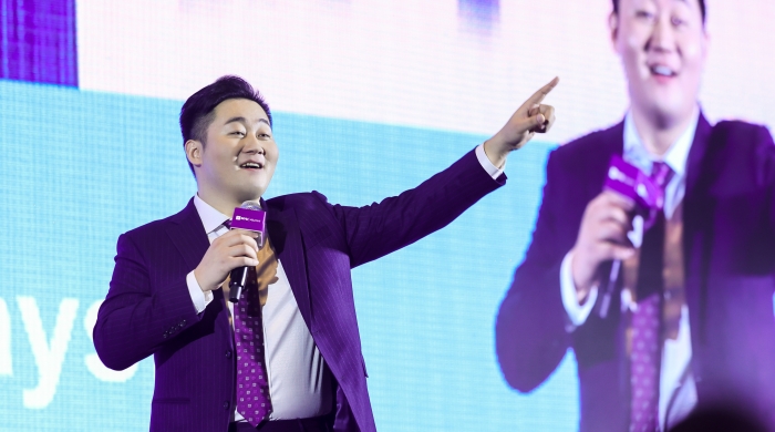Dongyang Fei on stage with microphone and large image of himself behind him