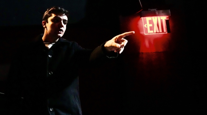 Student on dark stage pointing at lit up exit sign