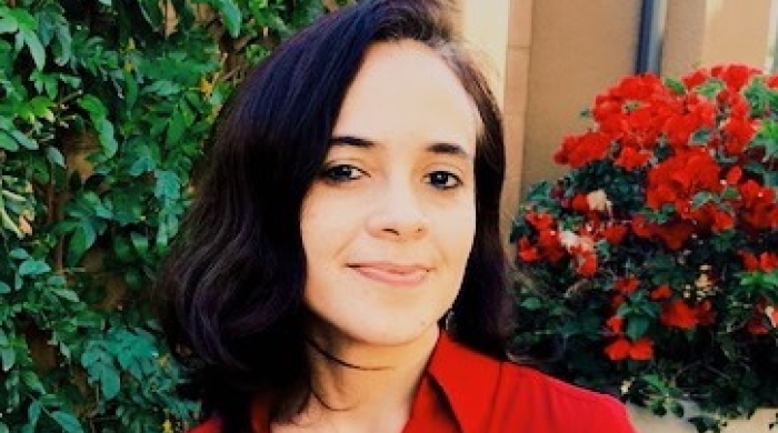 A picture of woman outside in a red blouse with dark hair smiling at the camera.