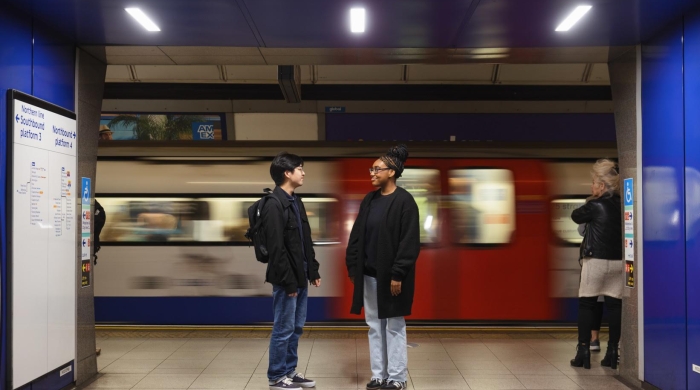 Two students standing beside a London subway car that is blurry from movement