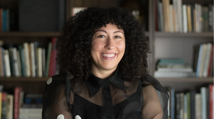 Christina is smiling in the center of the frame and has her arms crossed.