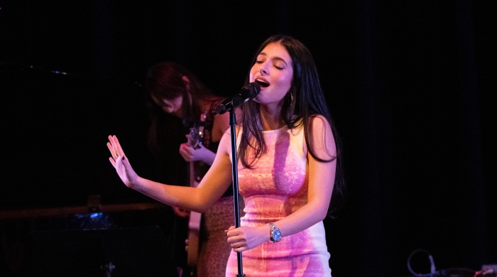 Student singing at mic on stage wearing a pink dress