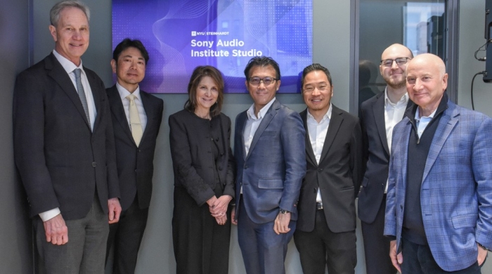 A group of 7 people stand in business clothing in front of a screen with NYU Steinhardt's logo and the text "Sony Audio Institute Studio"