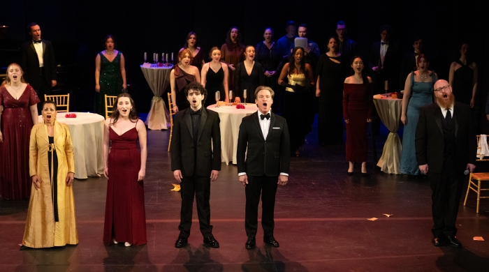 A row of opera singers with singers behind them readying to take a bow