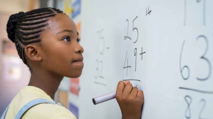 Black girl solving a math problem on a white board