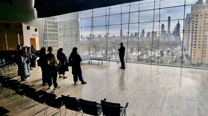 Students looking at the speaker in front of huge windows in Lincoln Center Apple Room.