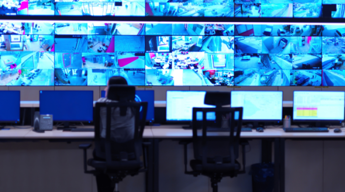 Person sitting at a desk looking at surveillance footage on various tv screens