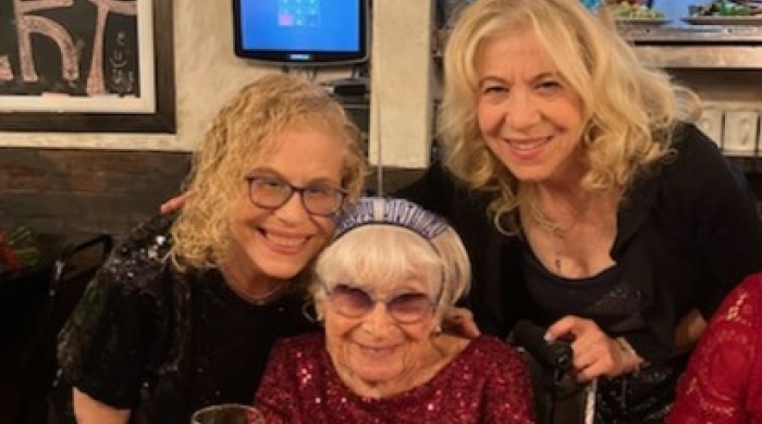 Dorothy sits at a table while two women pose with her