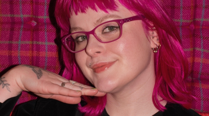 Student with raspberry colored hair posting in front of raspberry checked backdrop