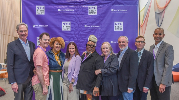 An event photo of nine people posting for the photo in front of an NYU Steinhardt step-and-repeat