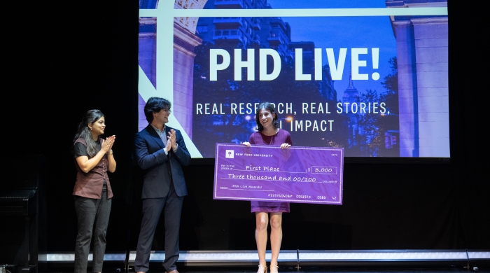 One student holds a large check while two others applaud