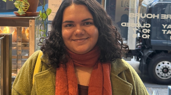 Photo of Laura Assanmal standing in a shop, wearing an orange scarf and green jacket