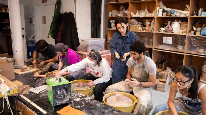 Students sit at wheels while the instructor looks over their work