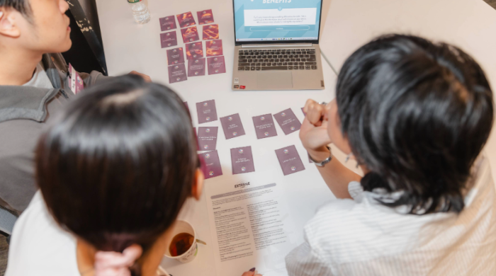 Students sit at a desk with cards and a laptop.