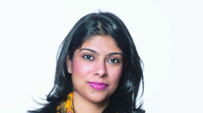 Manjari Sihare-Sutin, an Indian woman in a black shirt with a colorful scarf, looks into the camera with her arms crossed.