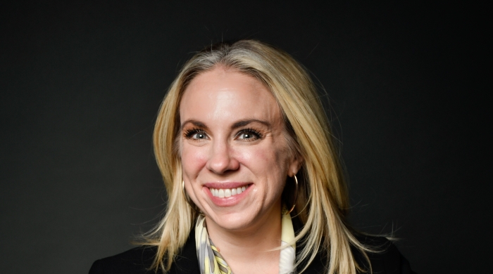 A white woman with blonde hair smiles into the camera.