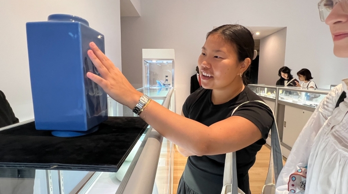 A smiling VAA student with reaches out to touch an art object in a gallery space.