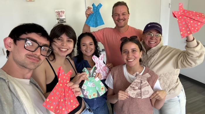A group of VAA students pose holding paper dresses in varying prints.