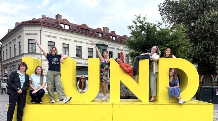 Students pose on and around a bright yellow sign reading "Lund"
